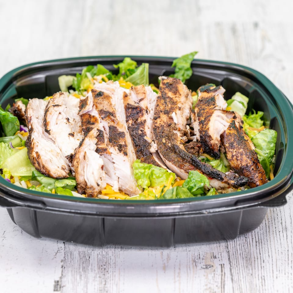 St. Bess Jerk's jerk chicken salad with lettuce, cheese, and sliced grilled chicken in a black container.