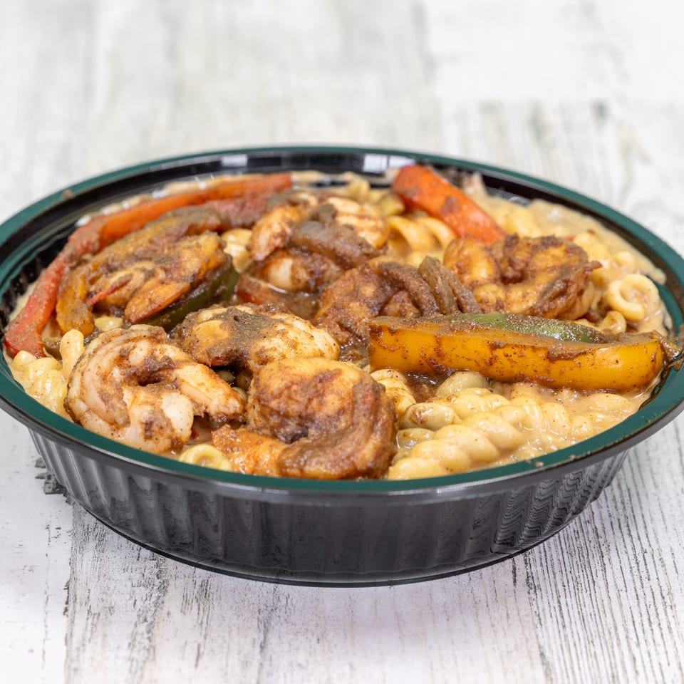 Jerk shrimp and bell peppers over creamy macaroni in a black bowl from St. Bess Jerk.
