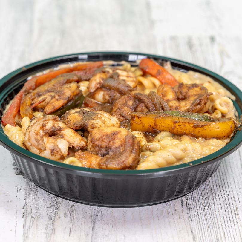 Jerk shrimp and bell peppers over creamy macaroni in a black bowl from St. Bess Jerk.