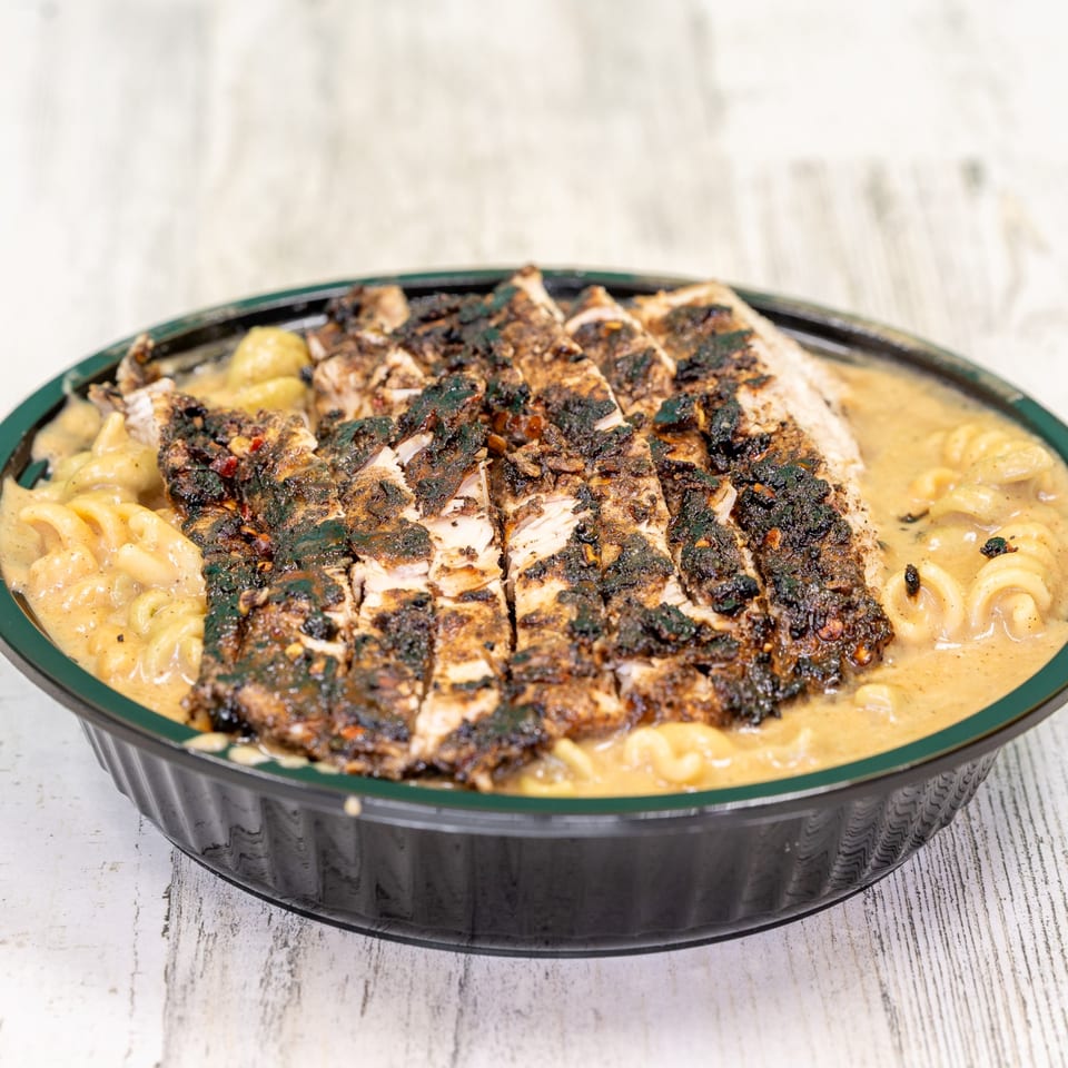 St. Bess Jerk's jerk chicken, sliced and served over creamy mac and cheese in a black bowl.