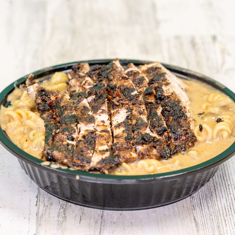 St. Bess Jerk's jerk chicken, sliced and served over creamy mac and cheese in a black bowl.
