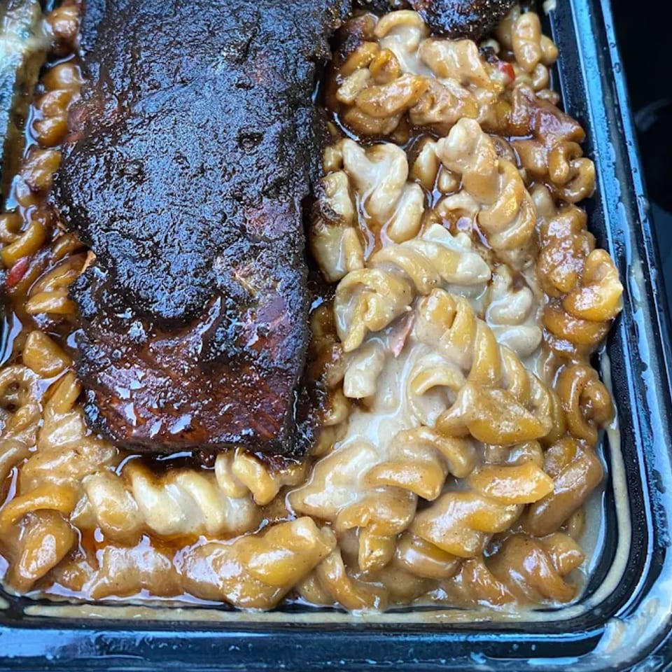 Close-up of St. Bess Jerk's jerk chicken and creamy mac and cheese in a black container.
