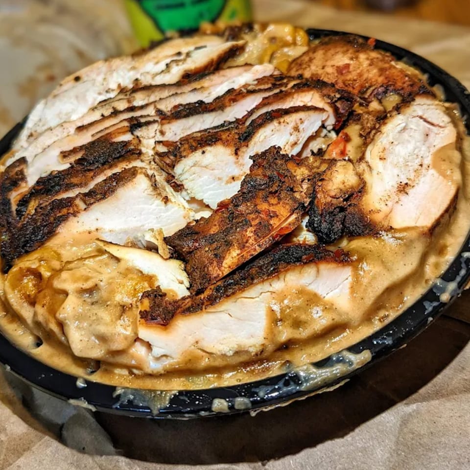 Close-up of St. Bess Jerk's sliced jerk chicken with sauce, served in a black bowl.