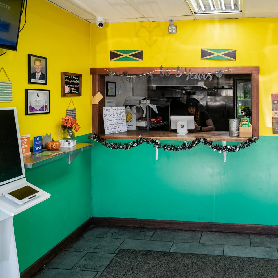 A vibrant yellow and teal interior of St. Bess Jerk, with a server behind the counter.